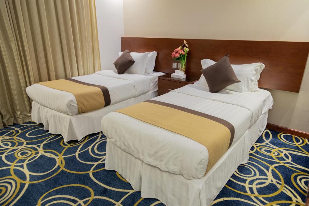 2 Betten in einem Hotelzimmer mit Blumen in der Unterkunft Carawan Hotel Jeddah in Dschidda
