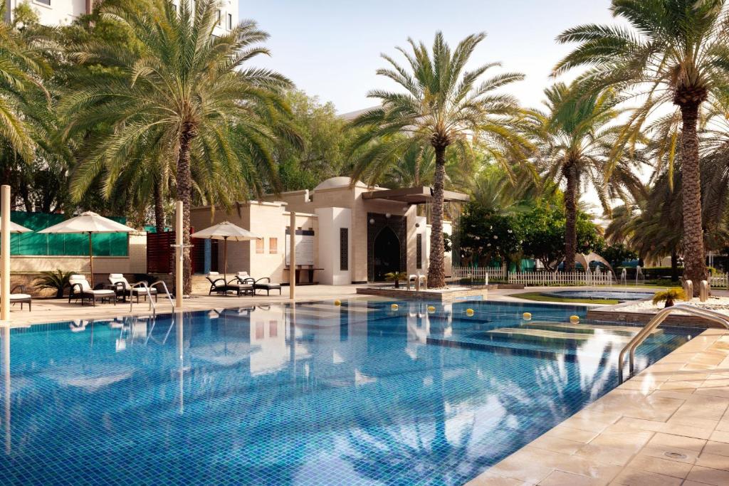 a large swimming pool with palm trees in the background at Sheraton Oman Hotel in Muscat