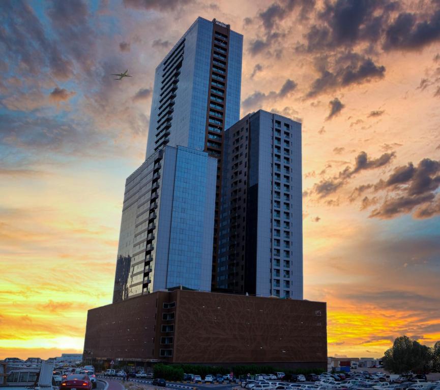 a tall building with a sunset in the background at Luxe Grand Hotel Apartments in Sharjah