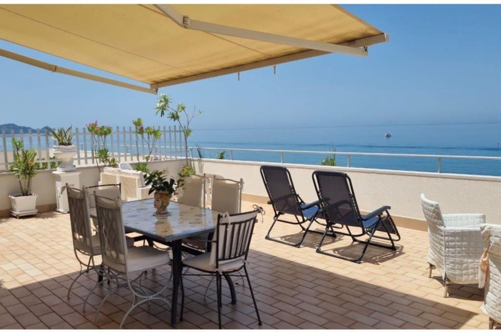 une terrasse avec une table et des chaises et l'océan dans l'établissement Attico una finestra sulle Isole Eolie, à Brolo