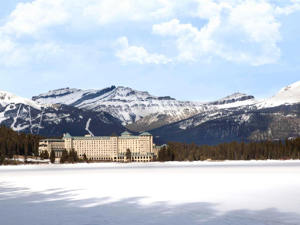 a hotel with snow covered mountains in the background at Fairmont Château Lake Louise in Lake Louise