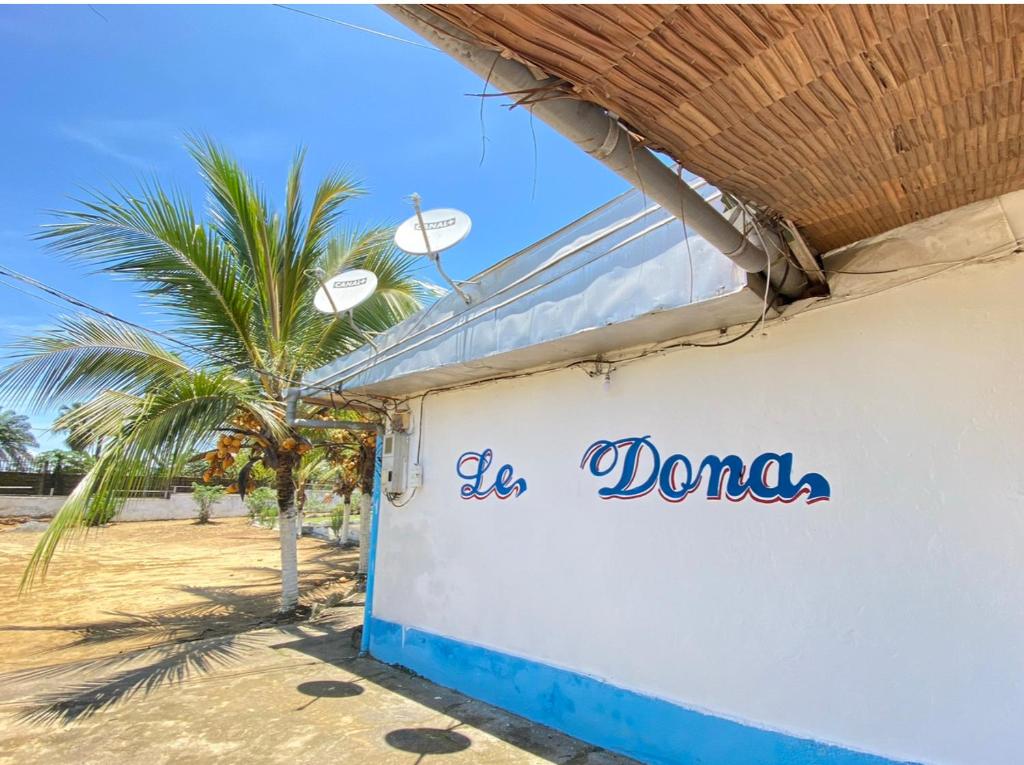 een witte muur met de woorden doana erop naast een palmboom bij Le Dona Kribi in Kribi