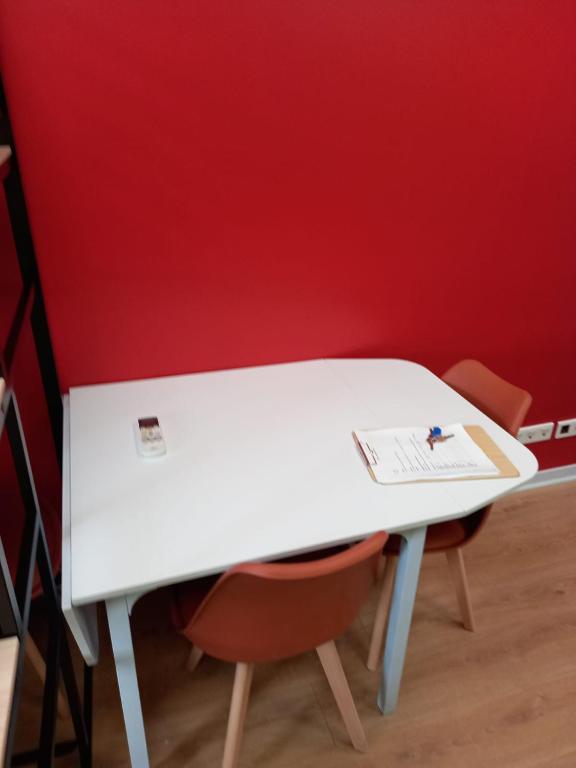 a white table with two chairs in front of a red wall at STUDIO AVEC TERRASSE DONNANT SUR UN PARC ABORE in Bourg-en-Bresse