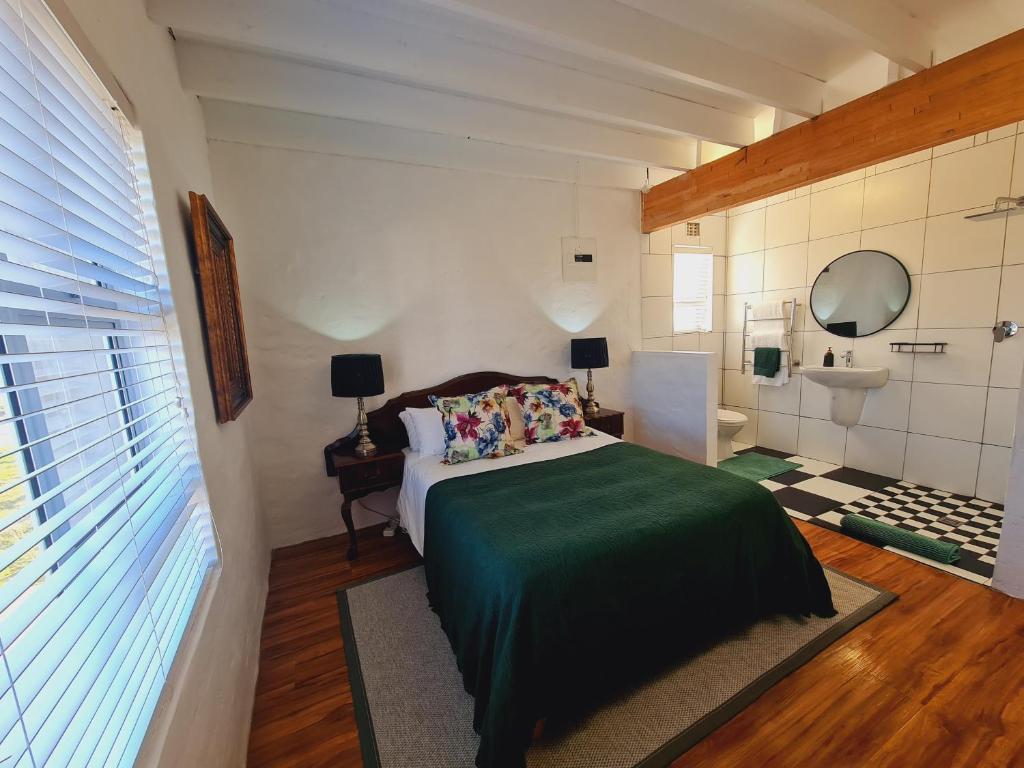 1 Schlafzimmer mit einem grünen Bett und einem Badezimmer in der Unterkunft Verregaande Cottage with hot tub in Agulhas