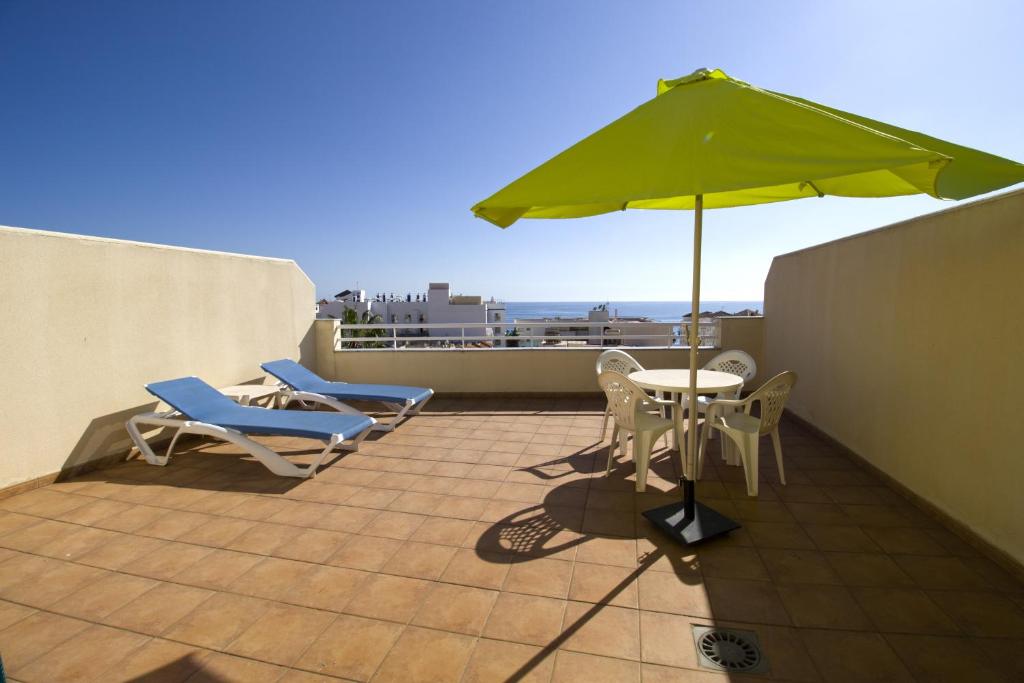 eine Terrasse mit einem Tisch, Stühlen und einem Sonnenschirm in der Unterkunft Apartamentos Turísticos Fercomar in Nerja