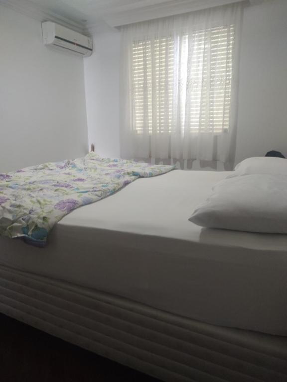 1 cama blanca en un dormitorio con ventana en Quarto em apartamento no centro de Blumenau !, en Blumenau
