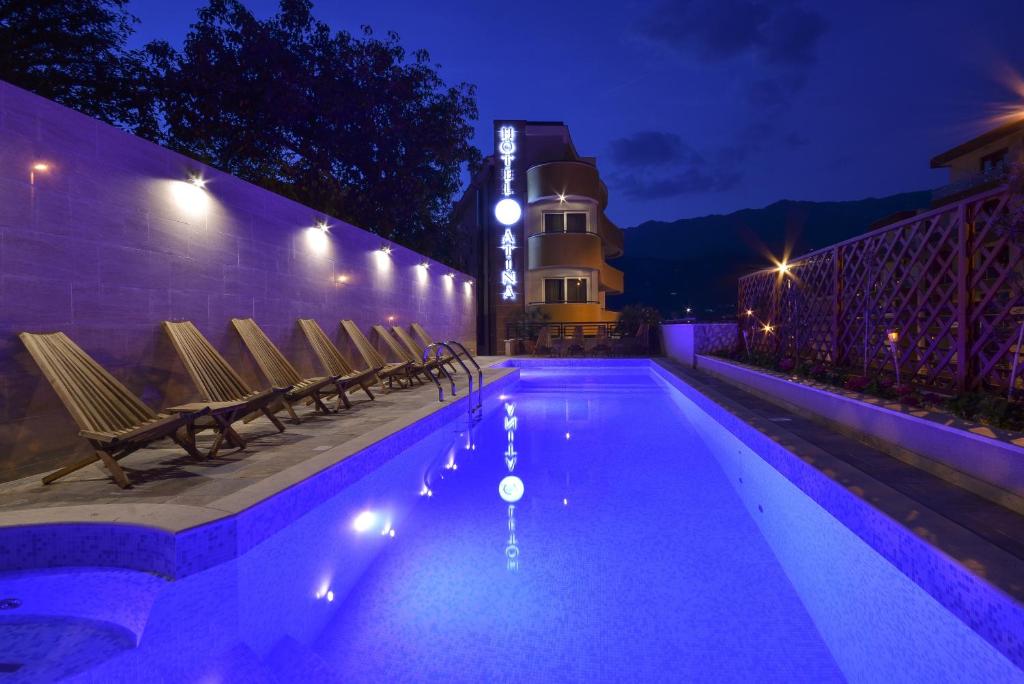 a swimming pool at night with chairs and a lighthouse at Hotel Atina in Budva