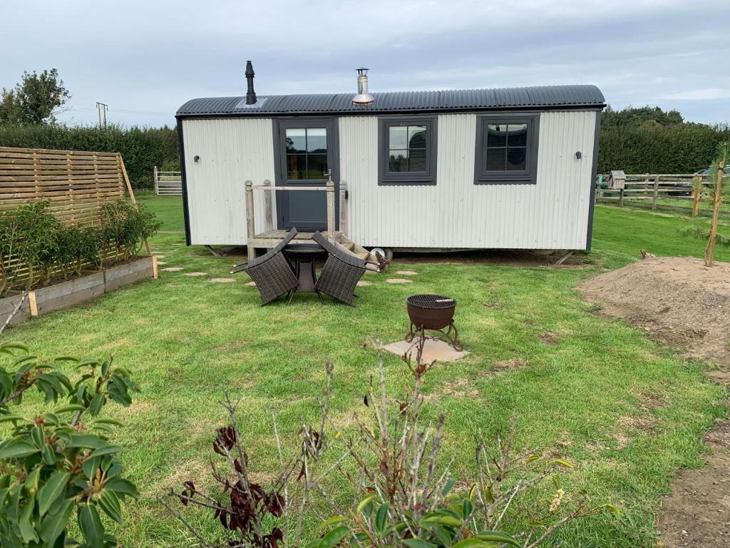 a small white shed with a table and chairs in a yard at Springwood Shepherd Huts Glamping York in York