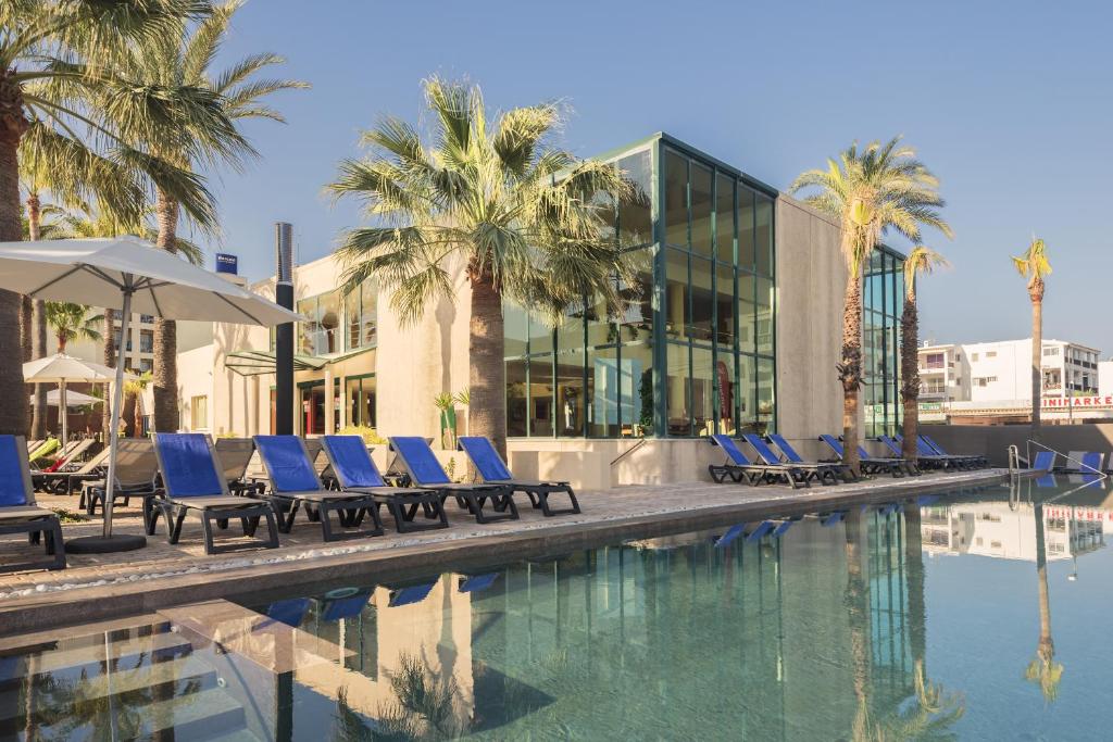 una piscina con tumbonas azules y palmeras en Occidental Ibiza, en Bahía de San Antonio