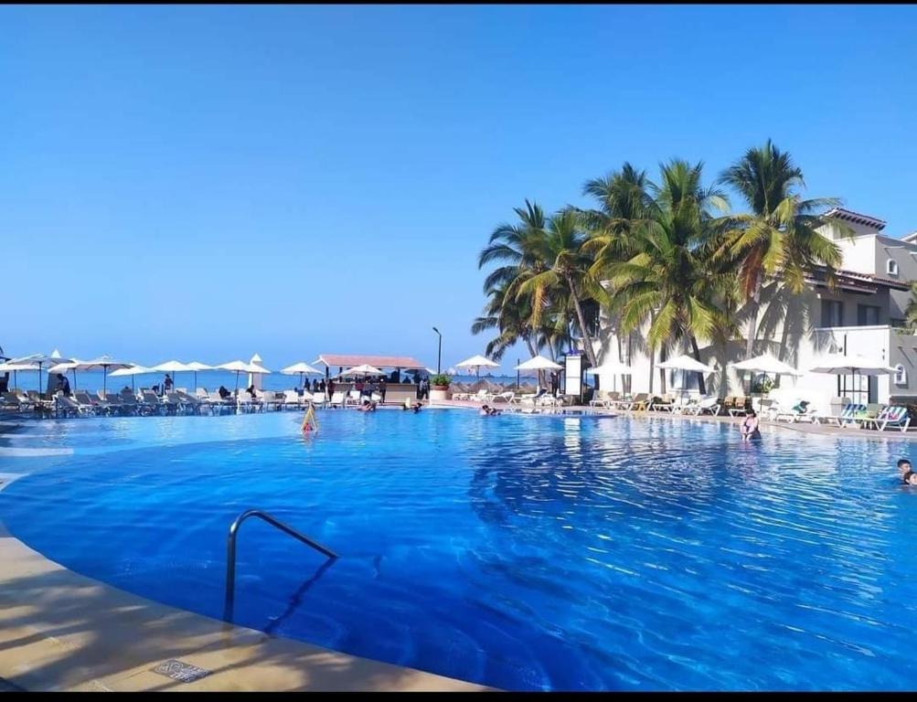 une grande piscine avec des palmiers et des personnes y séjournant dans l'établissement El mejor departamento a la orilla del mar, à Ixtapa