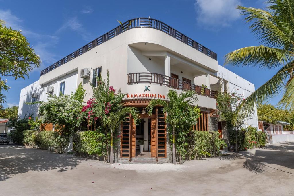 a white building with a balcony and palm trees at Kamadhoo Inn in Baa Atoll