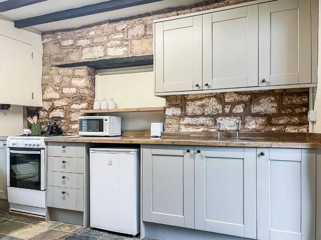 a kitchen with white cabinets and a stone wall at Meadow View Cottage in Highpeak Junction