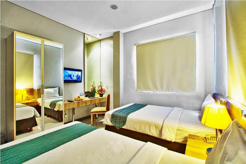 a hotel room with two beds and a mirror at Javein Griyadi Hotel in Jakarta