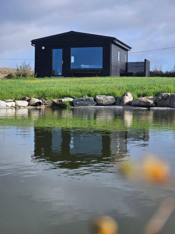 a black house sitting on top of a body of water at Wild Hideaways Luxury Lodges and Eco Spa in Bantry