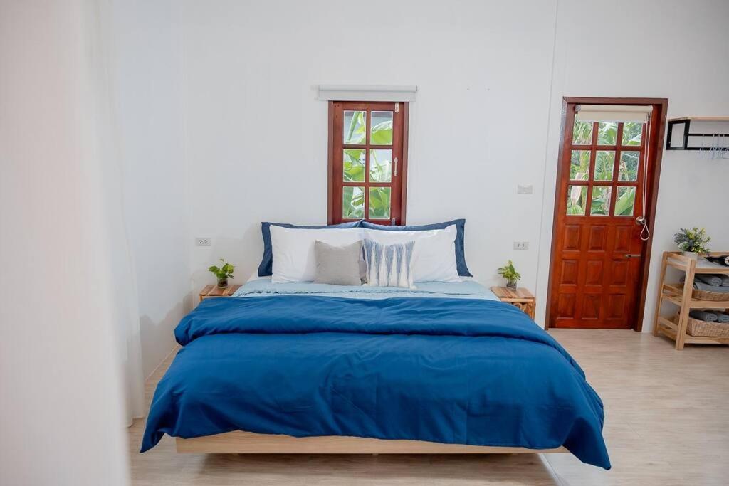 a bed in a white room with a blue blanket at Vawa Guesthouse in Kanchanaburi