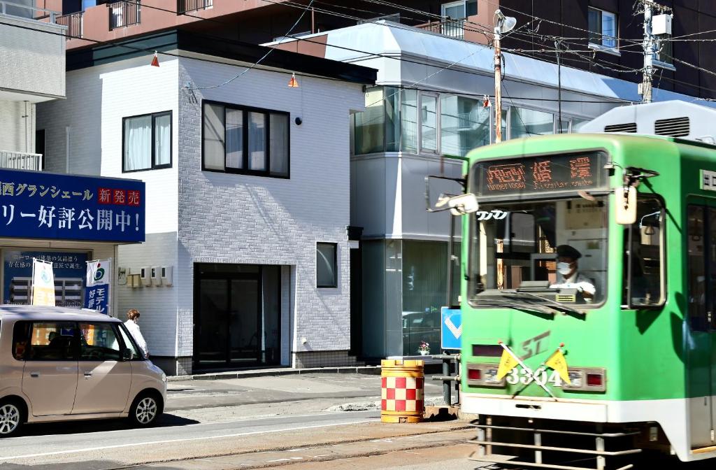a green bus driving down a street next to a building at Dream Tree 札幌市电步行0分钟 超市步行1分钟 in Sapporo