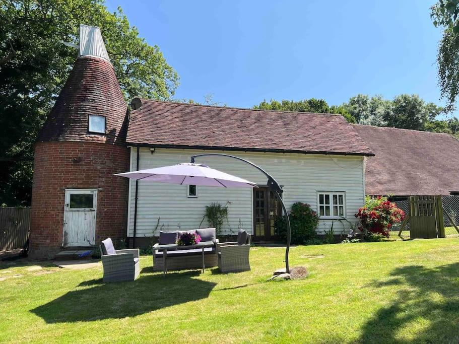 a house with an umbrella in front of a yard at Beautiful 2 bed Oast - 15 acre farm - Tunbridge Wells in Royal Tunbridge Wells