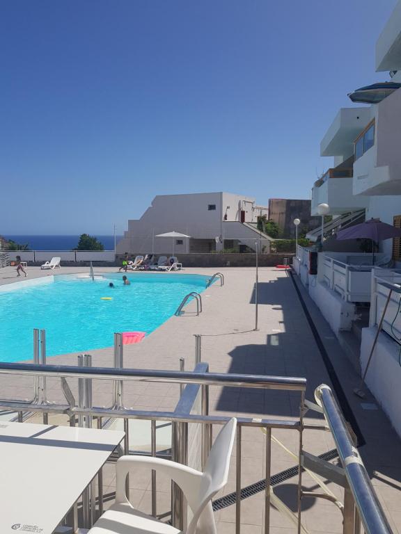 une piscine à l'eau bleue et des chaises blanches dans l'établissement Happy Arimar Apartments Puerto Rico, à Mogán