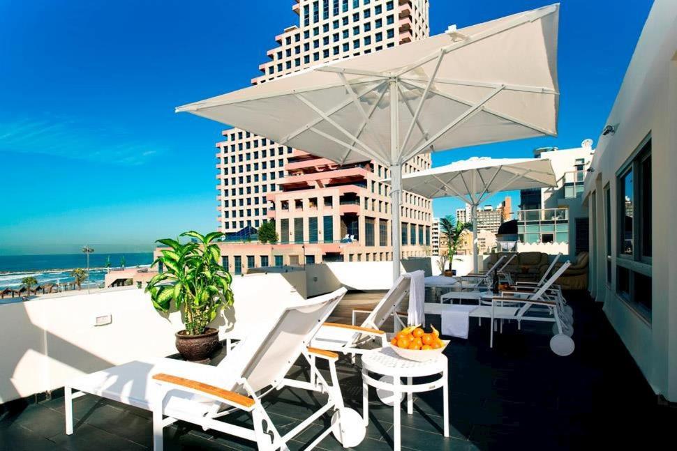 a balcony with white chairs and tables and an umbrella at Bell Boutique and Spa Hotel in Tel Aviv