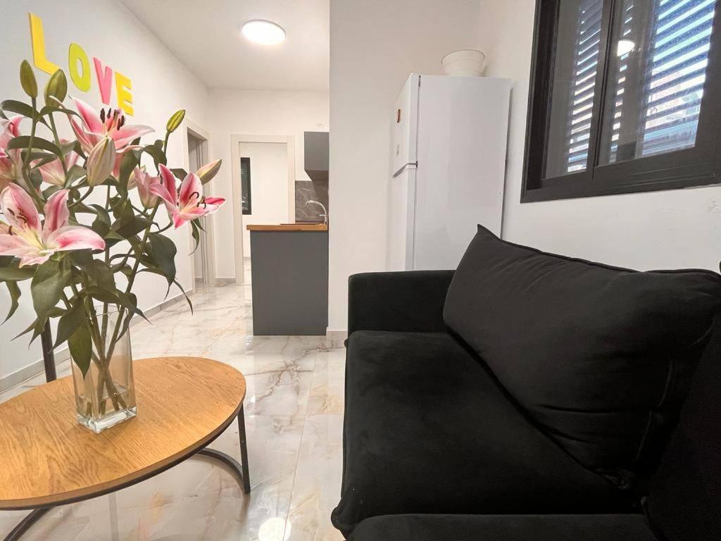 a living room with a black couch and a table with flowers at LEGOS APARTMENTS in Tel Aviv