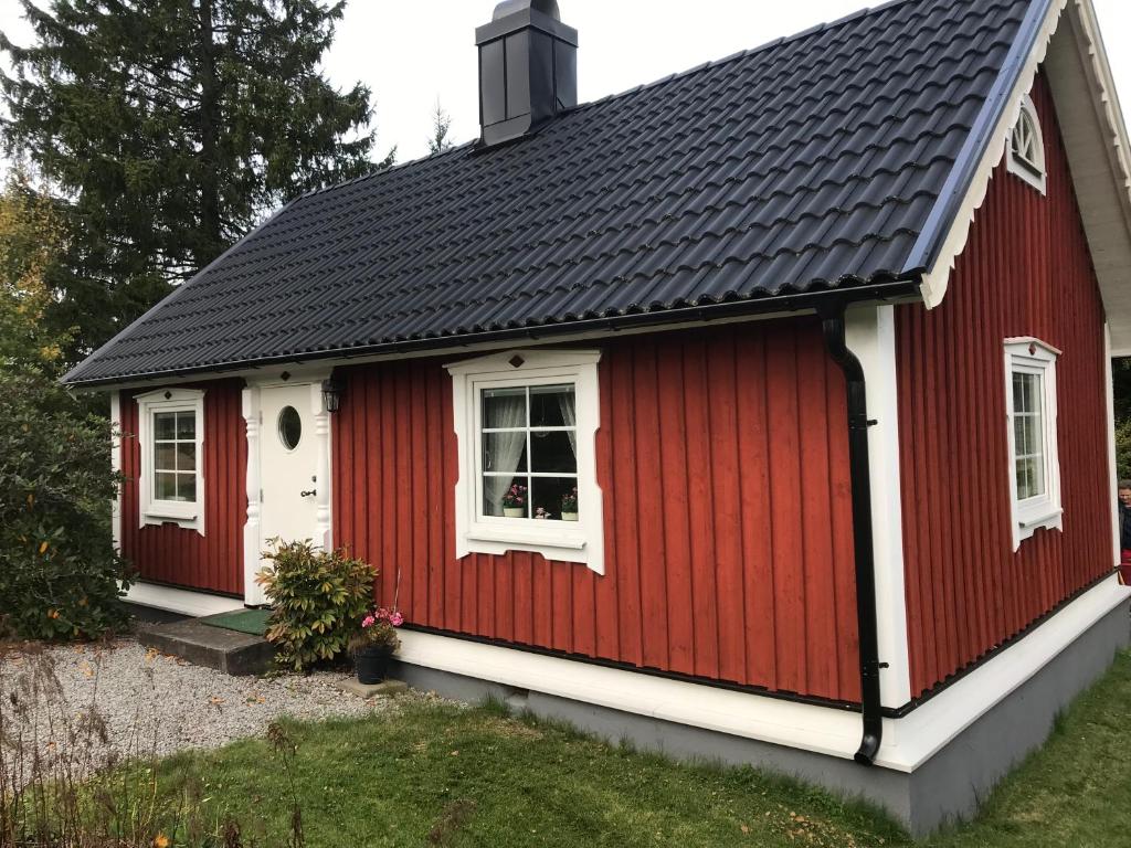 een rood huisje met witte ramen en een zwart dak bij Gulliga torpet in Vislanda