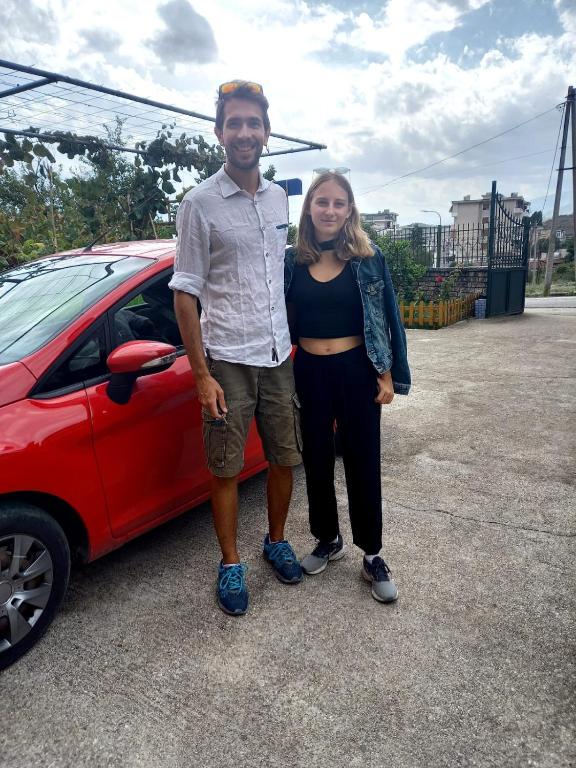 a man and a woman standing next to a red car at GuestHouseMantho in Gjirokastër