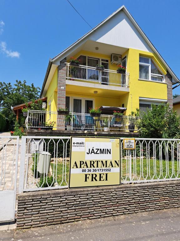 a yellow house with a sign on a fence at Jázmin Apartman Zalakaros in Zalakaros