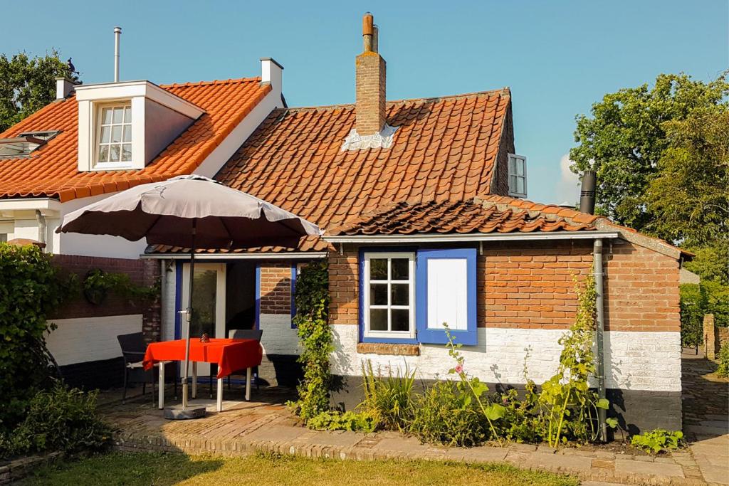 uma pequena casa com um guarda-sol, uma mesa e cadeiras em Countryside Bliss: Historic Cottage by the Sea em Burgh Haamstede
