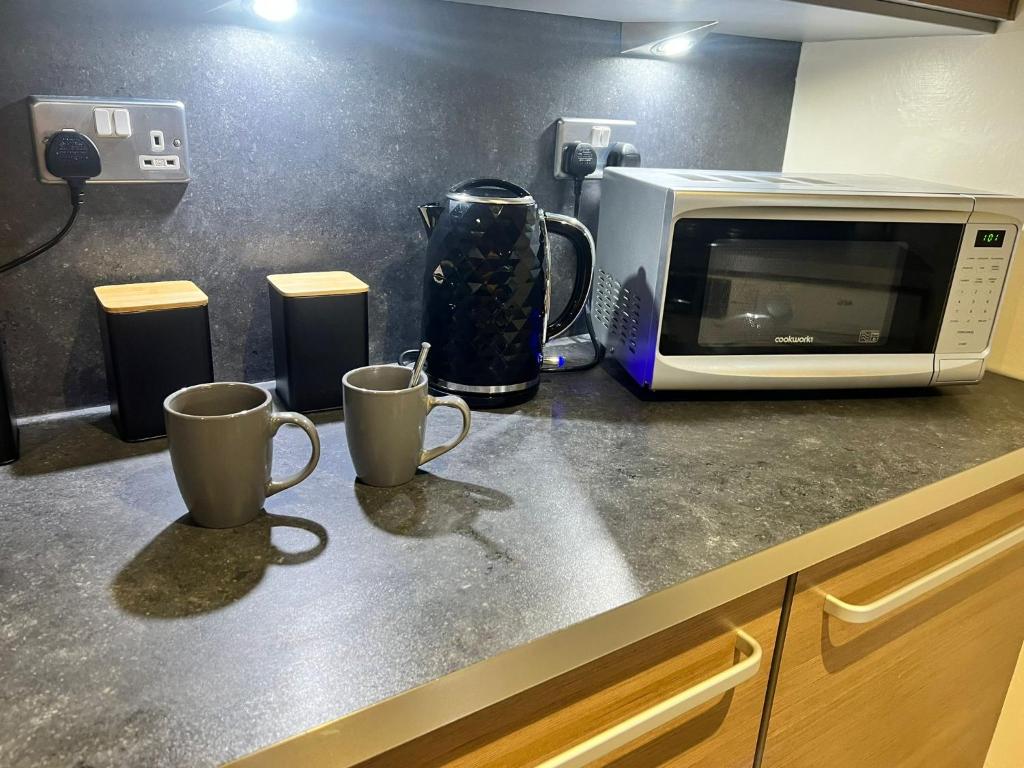 two coffee mugs on a counter next to a microwave at Pinecone Cottage in Frodingham