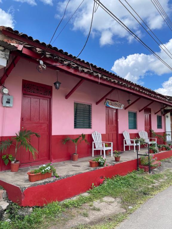 ein rosafarbenes Haus mit weißen Stühlen und einer roten Tür in der Unterkunft Hostal Voyager La Villa de Los Santos, Panama in Los Santos