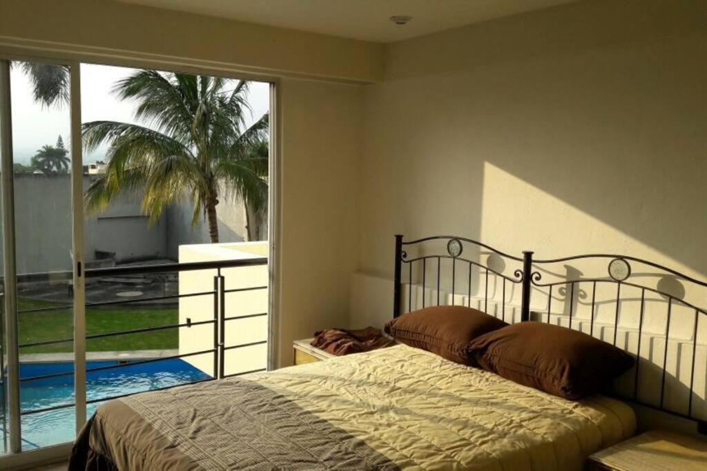 um quarto com uma cama e uma varanda com uma palmeira em Villa Colibri Casa Vacacional alberca asador jardín 15 huéspedes em Temixco
