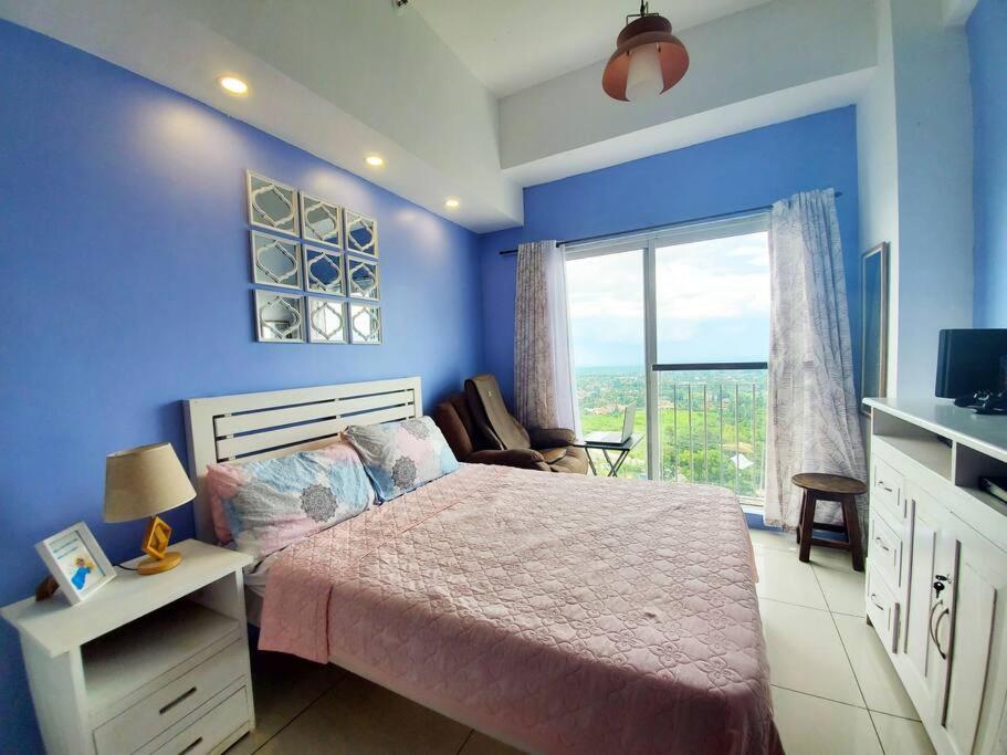 a blue bedroom with a bed and a large window at Sofias Place w/ Massagechair in Tagaytay