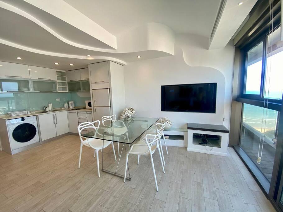 uma cozinha com uma mesa de vidro com cadeiras e uma televisão em ruth’s balcony sea view apt em Herzliya B