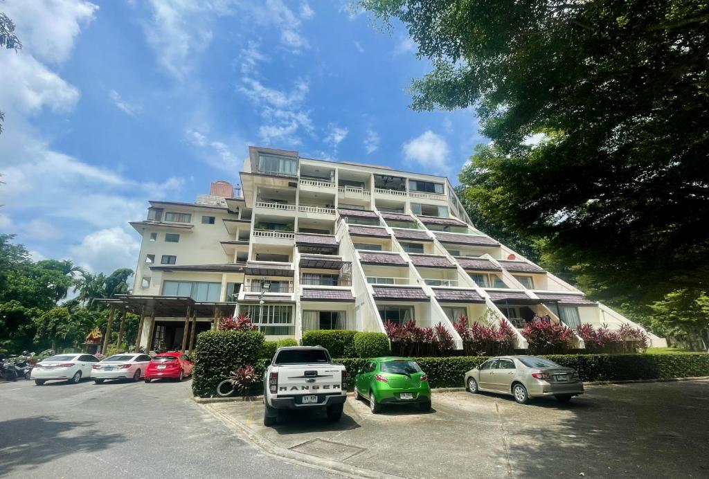 un gran edificio con coches estacionados en un estacionamiento en The Green Golf Apartments en Ban Thung Thong