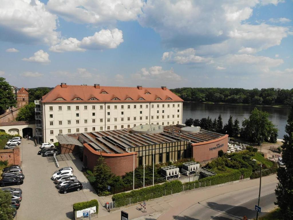 a large white building with a red roof next to a river at Hotel Bulwar in Toruń