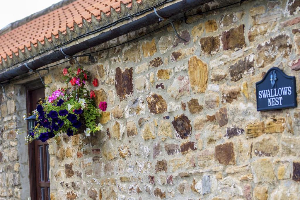 un cartel en una pared de piedra con una cesta de flores en Swallows Nest Holiday Cottage, en Cockfield