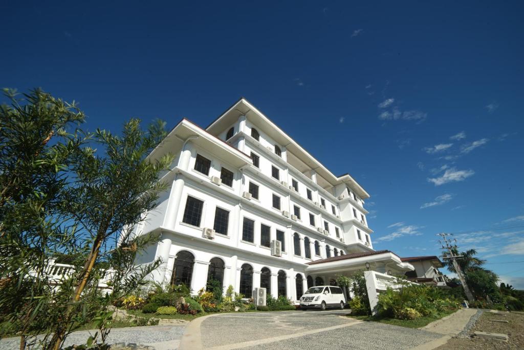 Biały budynek z samochodem zaparkowanym przed nim w obiekcie Isla De Oro Hotel w mieście Mamburao