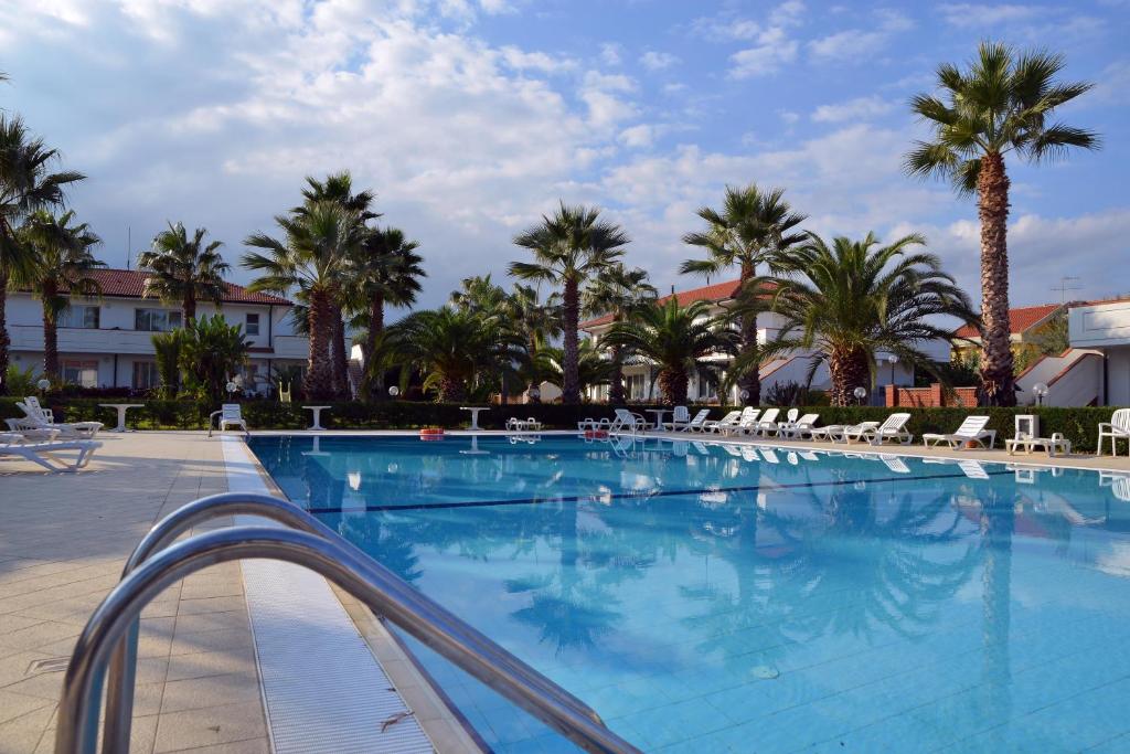 a large swimming pool with chairs and palm trees at King's House Hotel Resort in Mascali