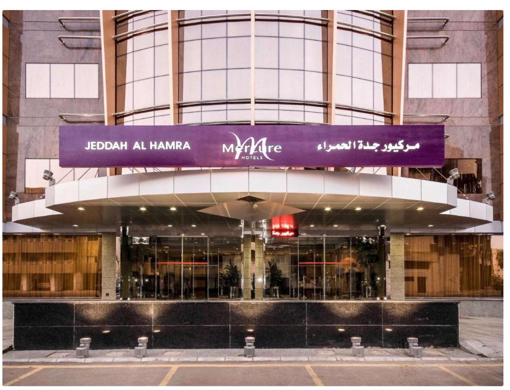 Mercure Jeddah Al Hamraa Hotel في جدة: مبنى أمامه لوحة أرجوانية