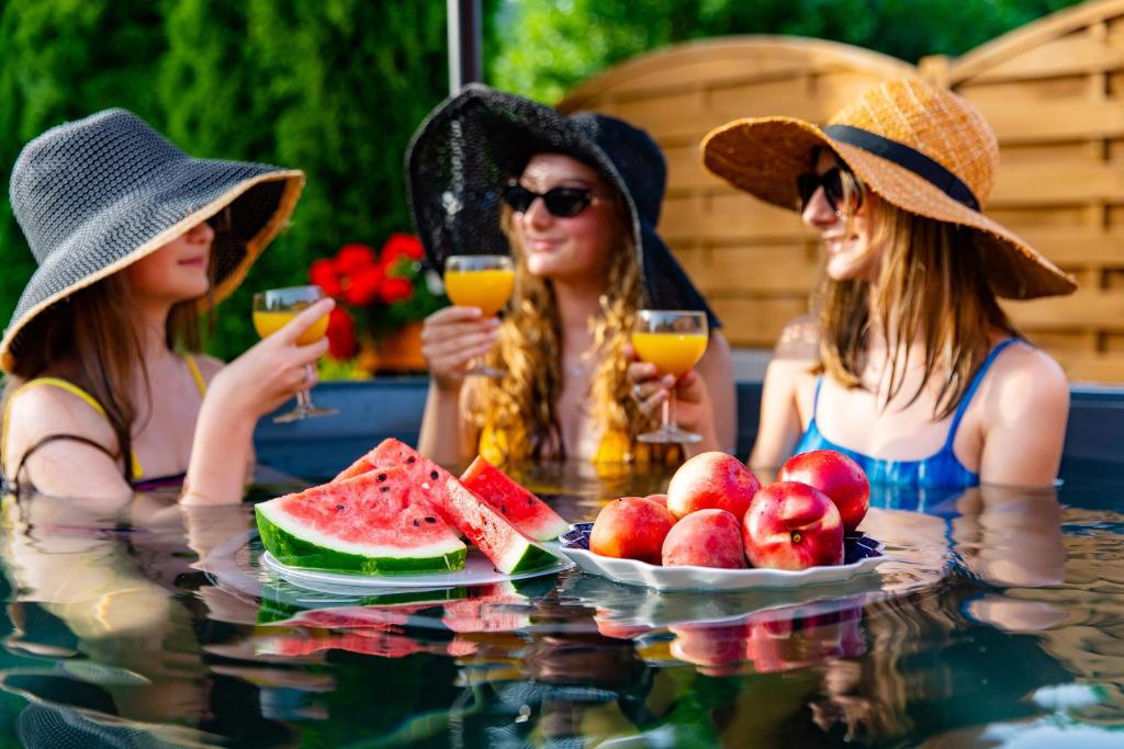 ノヴィ・タルクにあるWilla Biała Magnoliaの三人の帽子をかぶった女性が果物を持ってテーブルの周りに座っている