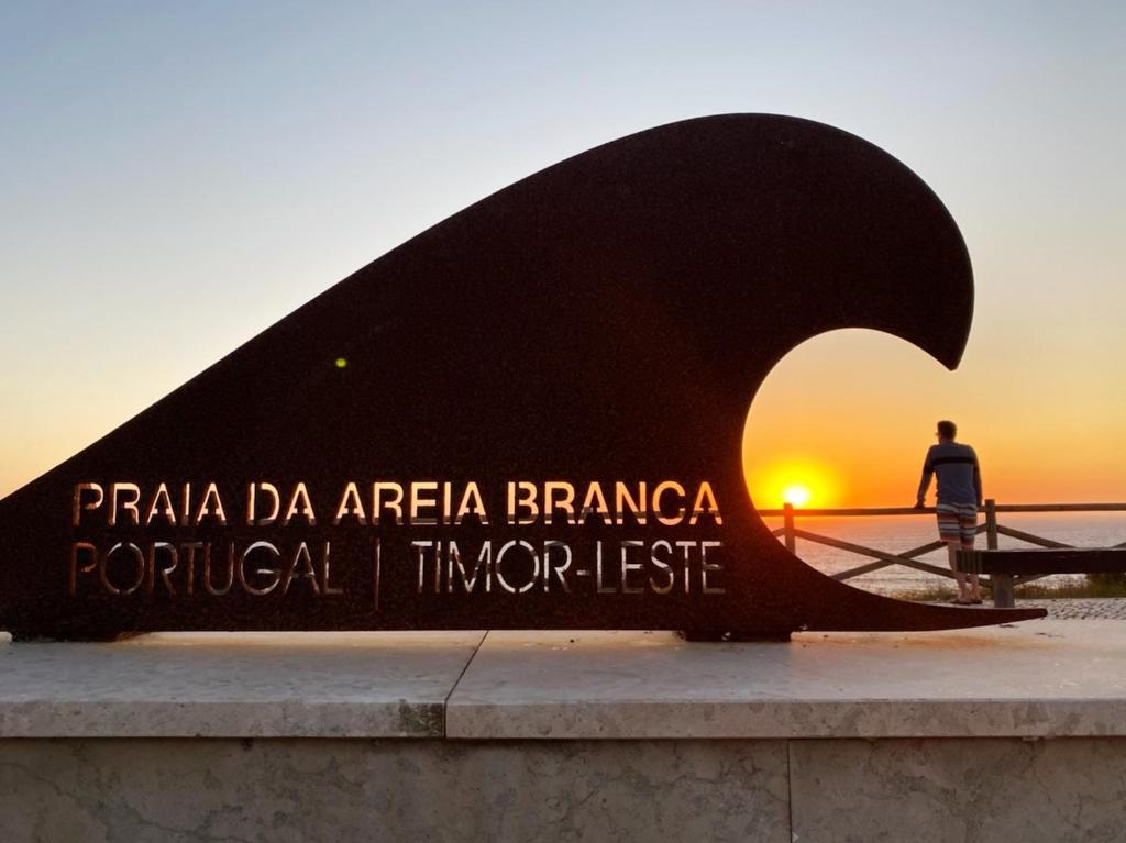 un homme debout devant une sculpture au coucher du soleil dans l'établissement Villa Surf Vista - Praia da Areia Branca, à Lourinhã