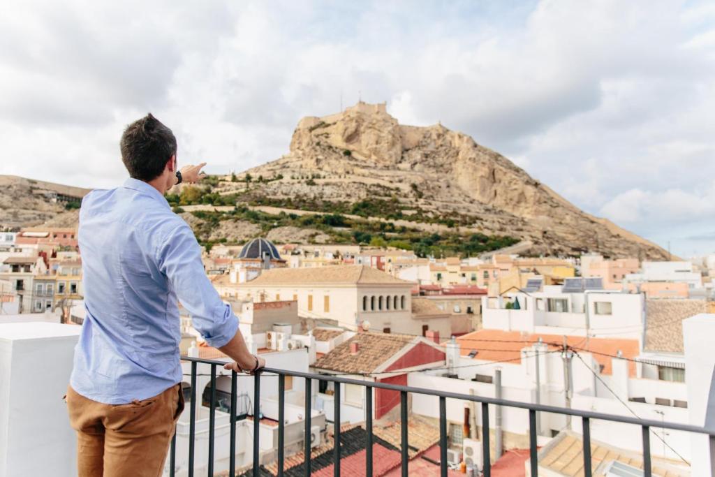 un hombre parado en un balcón mirando a la ciudad en Apartamentos Tito San Nicolas, en Alicante