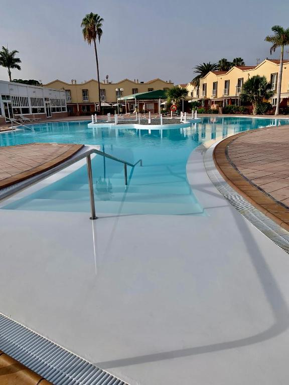 a large swimming pool with blue water and white chairs at Bungalow Green Oasis 1010 in Maspalomas
