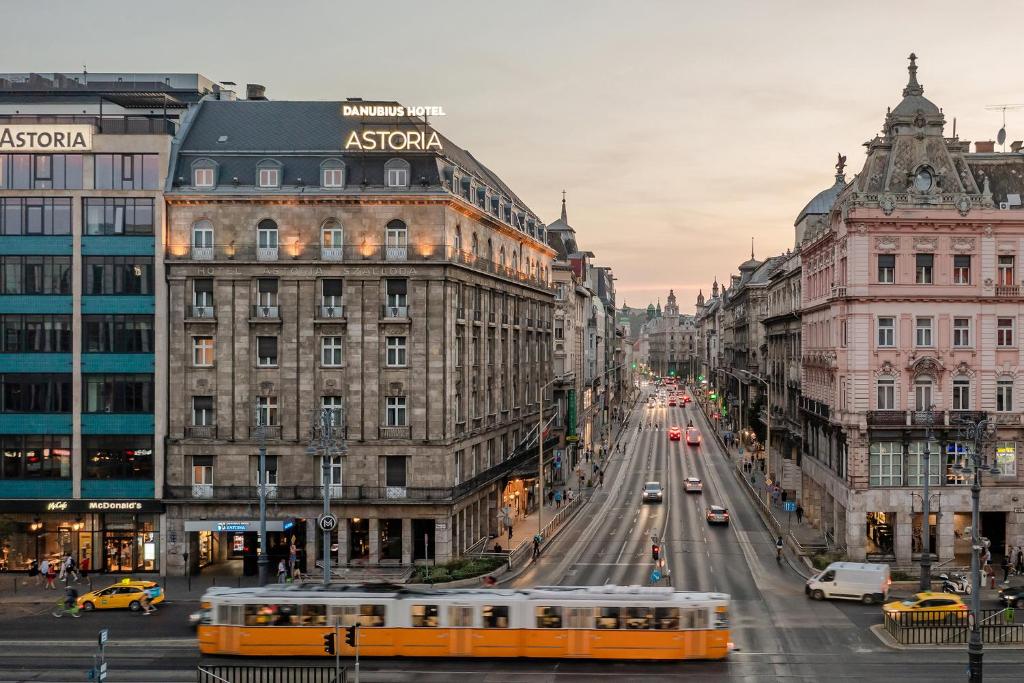a yellow bus driving down a city street with buildings at Danubius Hotel Astoria City Center in Budapest