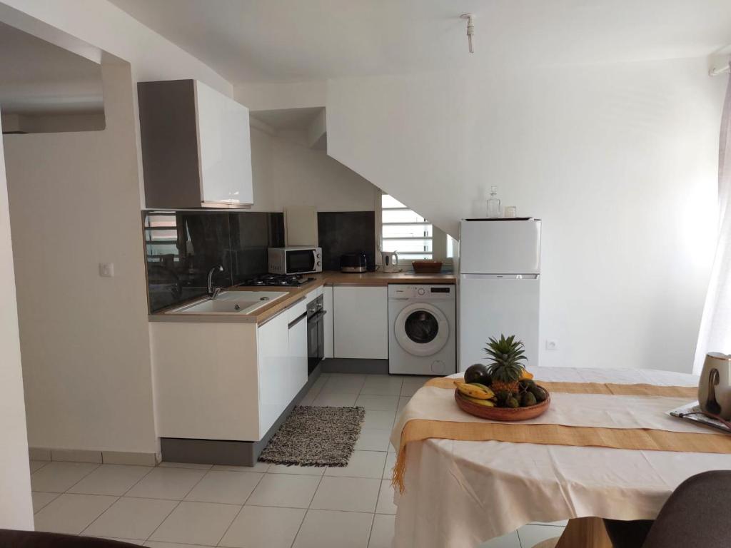uma cozinha com electrodomésticos brancos e uma mesa com uma tigela de fruta em Balaou em Les Anses-dʼArlets