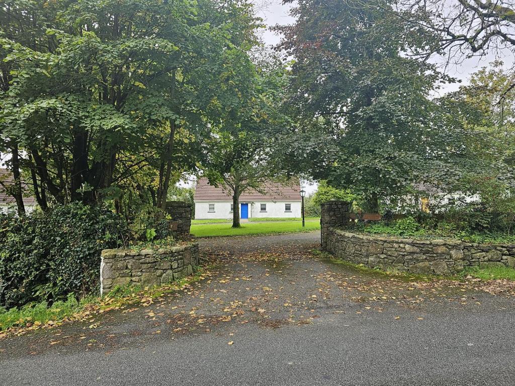 uma entrada com uma cerca de pedra e árvores e uma casa em Longford Holiday Blue Sky Self Catering Cottage 
