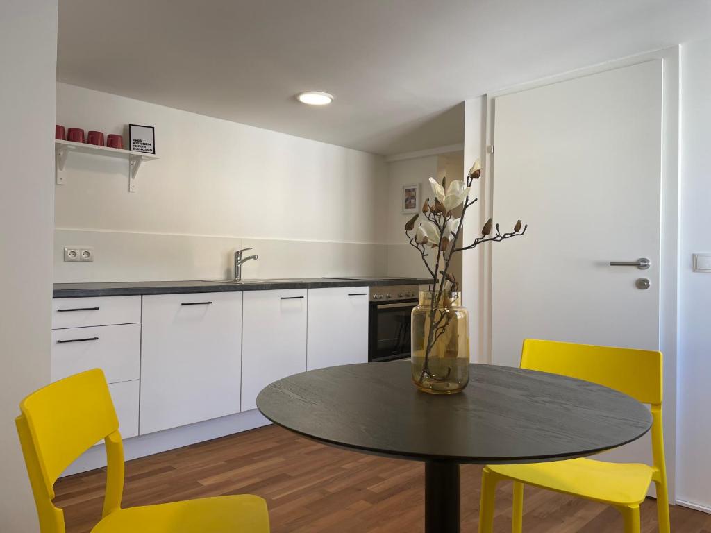 a kitchen with a table with yellow chairs and a vase with flowers at Modernes Stadtleben im gemütlichen City Apartment Dornbirn, London 8 in Dornbirn