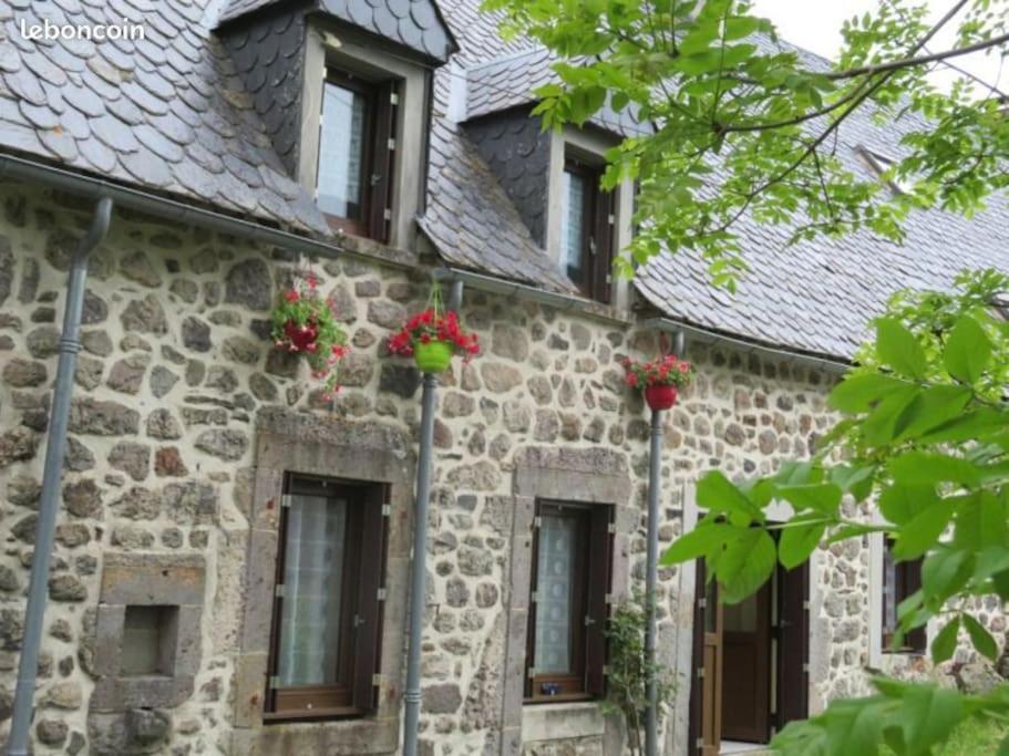 uma antiga casa de pedra com flores nas janelas em Maison au cœur du Sancy em Férérolles