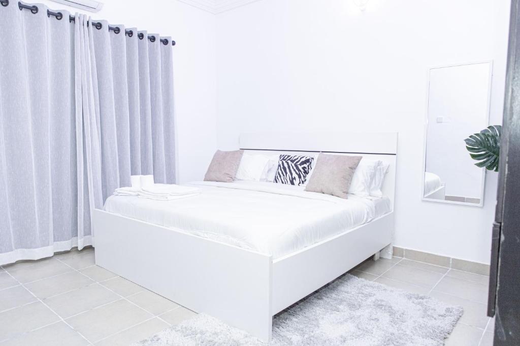 un letto bianco in una camera bianca con tende di Novara Apartments a Lekki