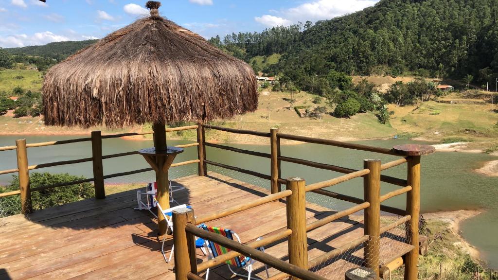 a wooden deck with a straw umbrella and a body of water at Chácara Bela Vista in Paraibuna